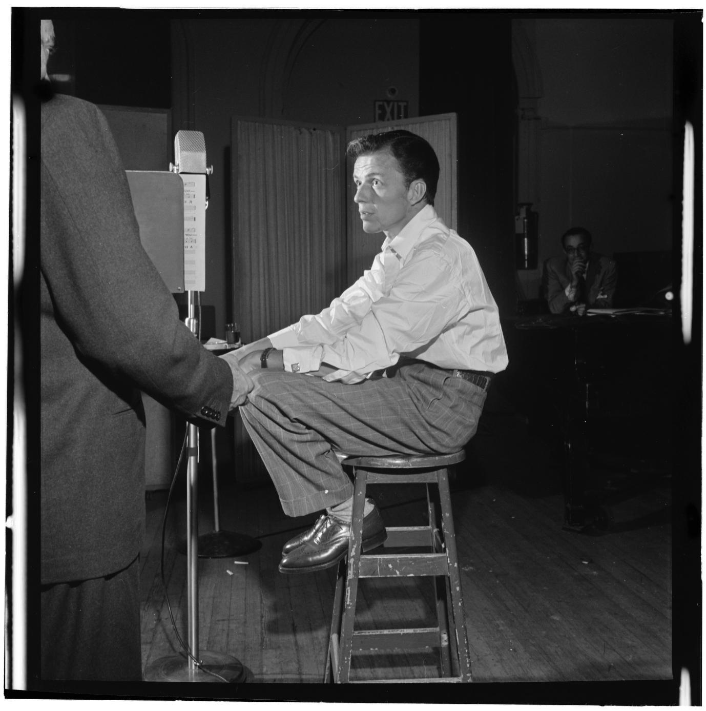 Frank Sinatra seated on a tall stool beside a microphone and music stand at Liederkrantz Hall, circa 1947.