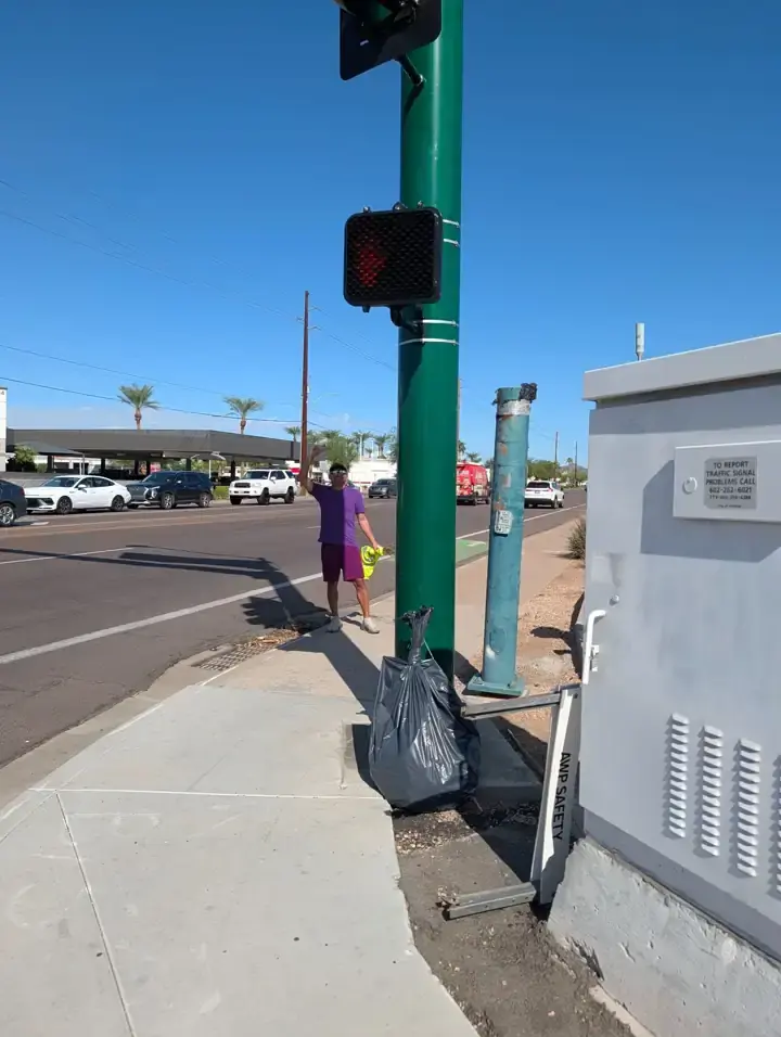 One volunteer at the 20th Street crossing, with a collected trash bag near the signal pole