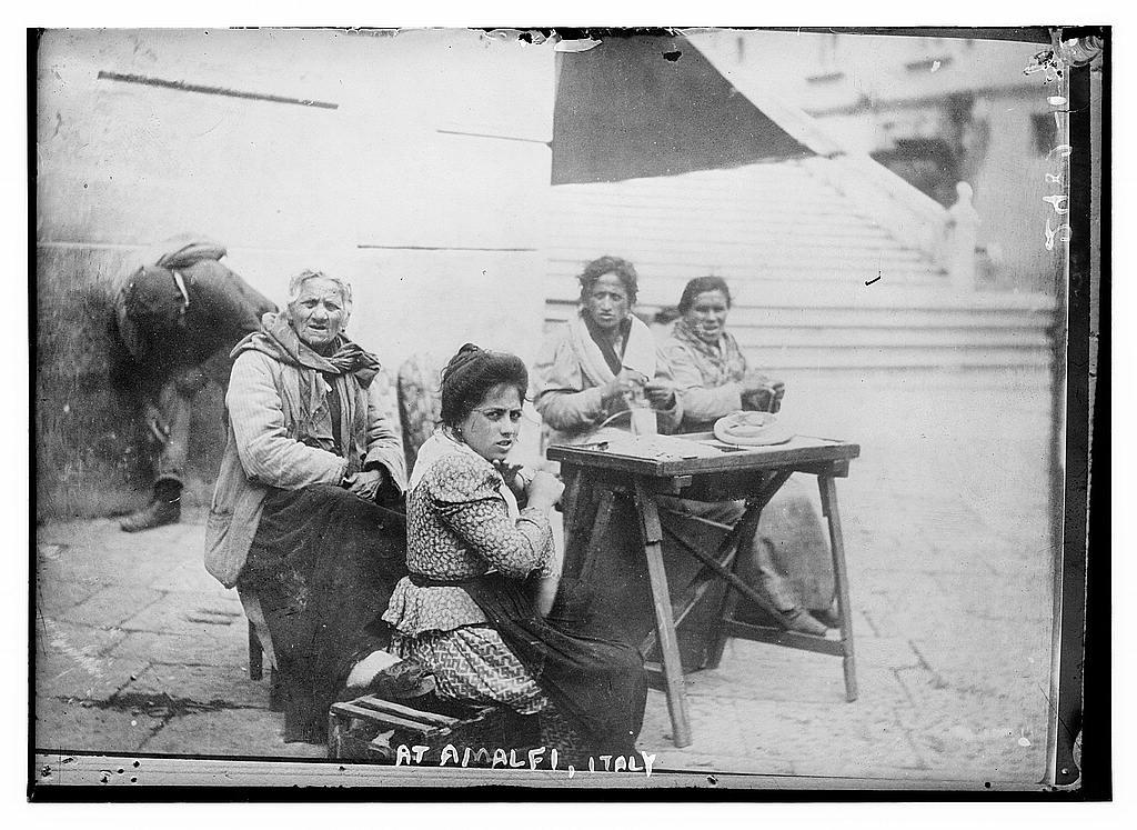 People seated outdoors in the historical photograph cataloged as At Amalfi, Italy.