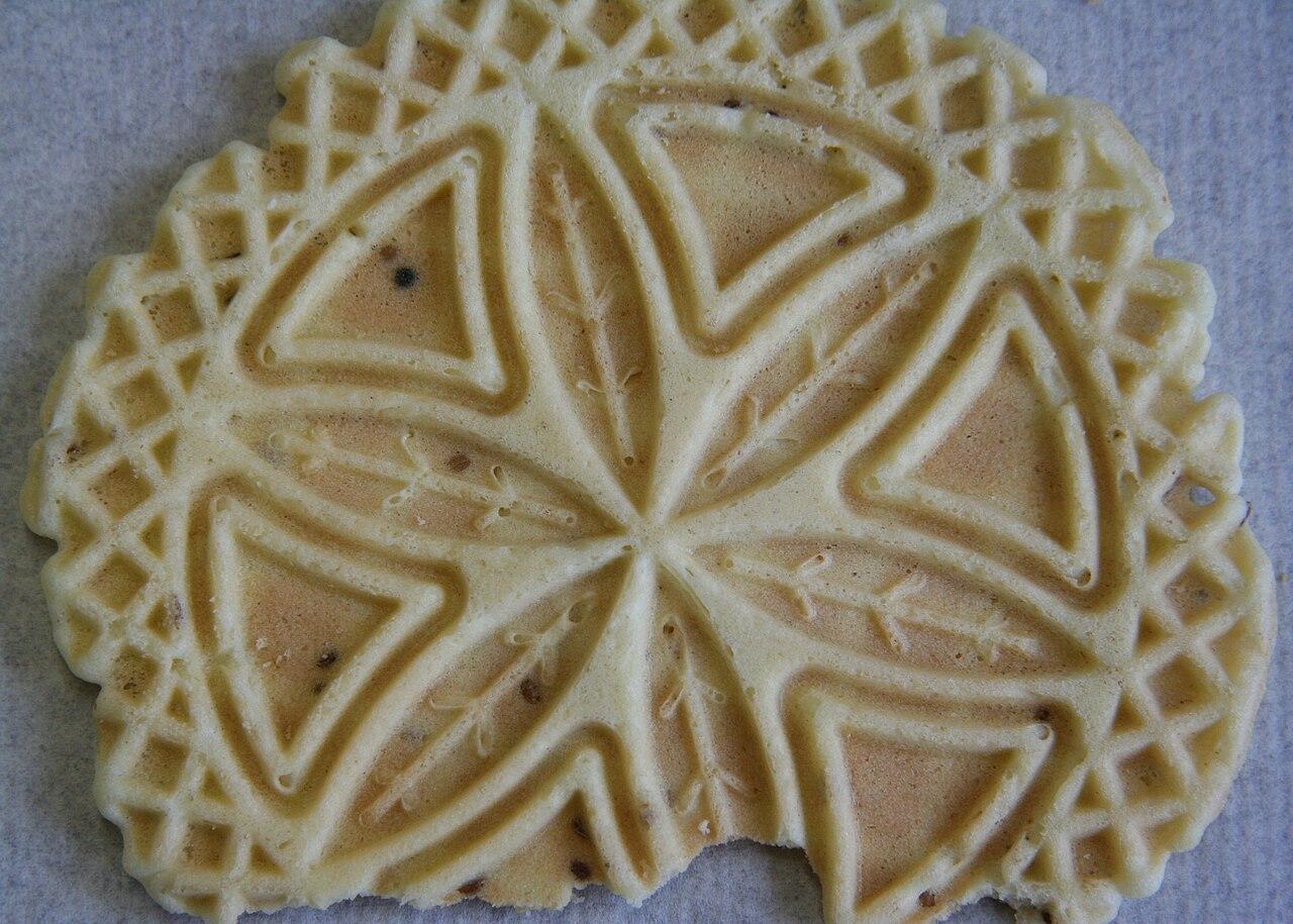 A close view of a patterned pizzelle cookie with a scalloped edge.