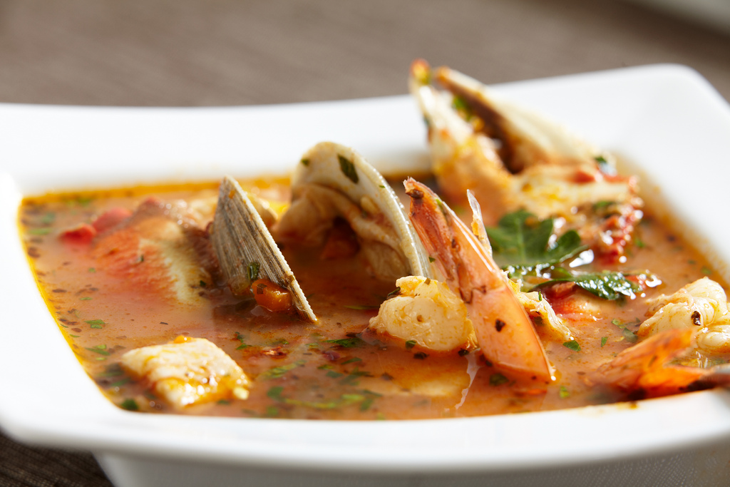Shrimp and clams in orange-red cioppino broth, served in a white bowl.