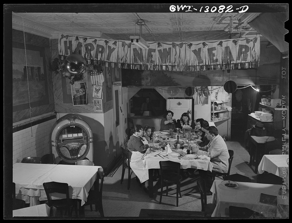 The Di Costanzo family seated around a restaurant table beneath New Year decorations, with a jukebox to the left.