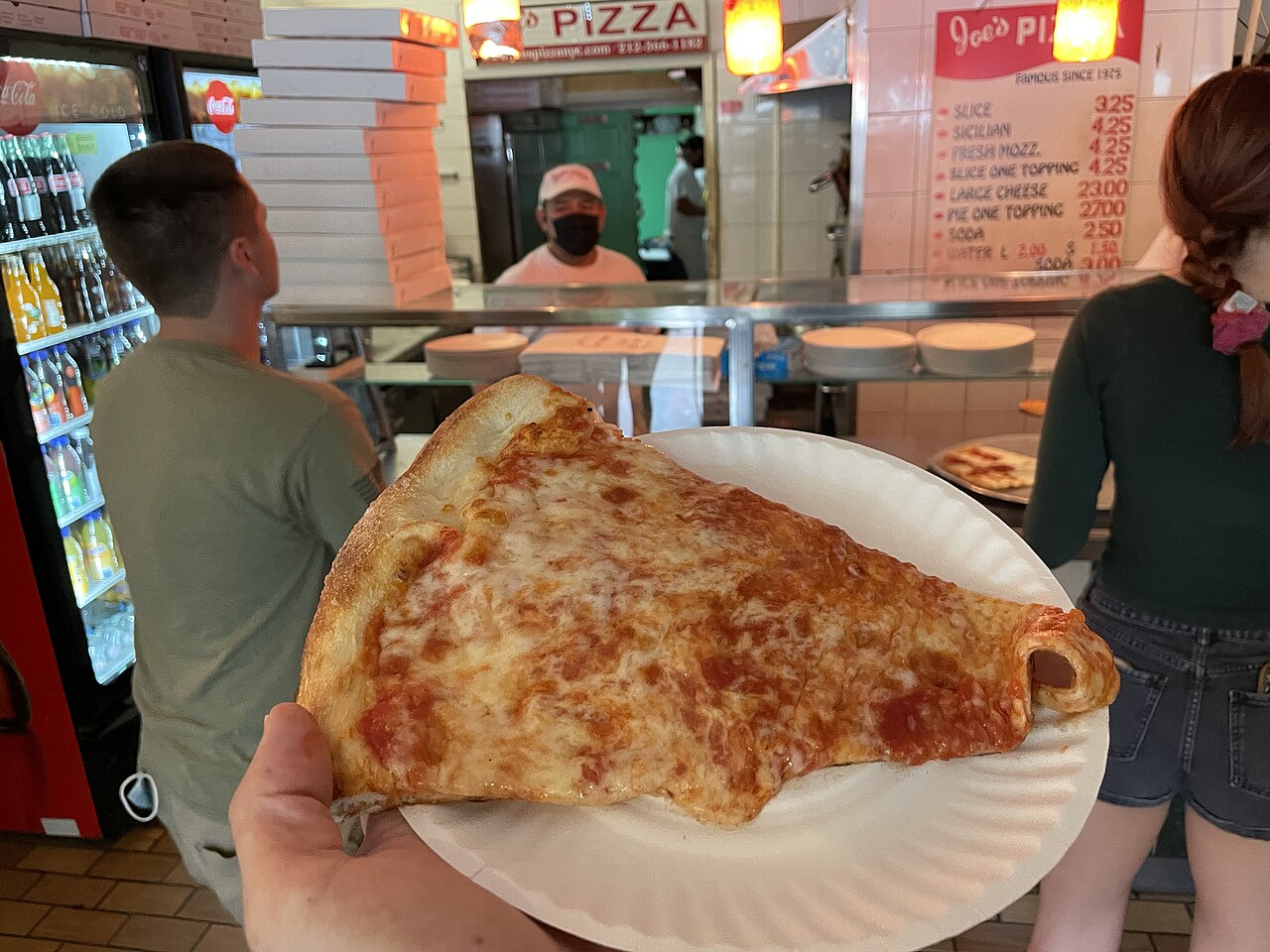 A large cheese pizza slice on a paper plate inside Joe’s Pizza in Manhattan
