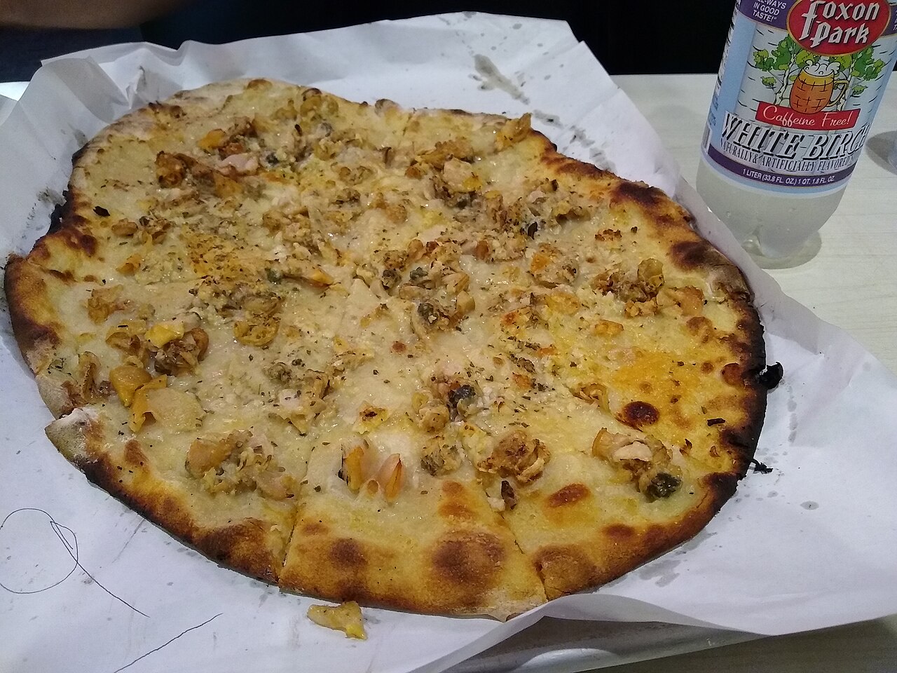 White clam pizza with a charred crust at Frank Pepe’s in New Haven, beside a bottle of Foxon Park soda